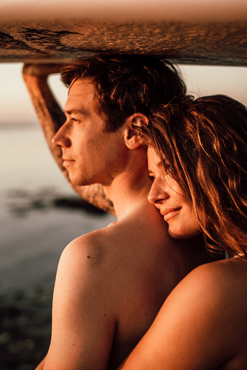Frau legt ihren Kopf auf die Schulter ihres Partners und schaut sich mit ihm gemeinsam den Sonnenuntergang an