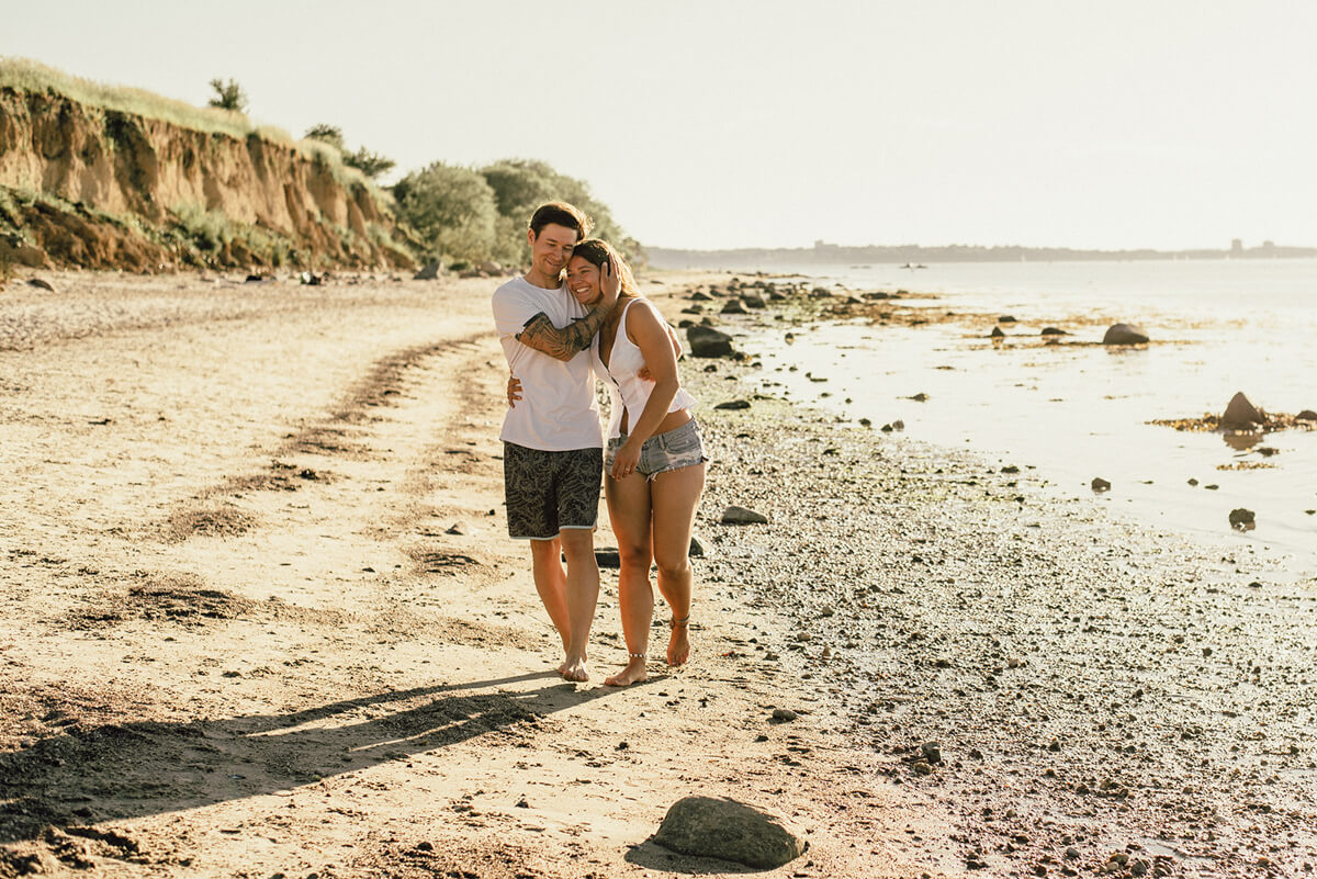 Paar läuft Arm in Arm am Strand entlang und ist glücklich